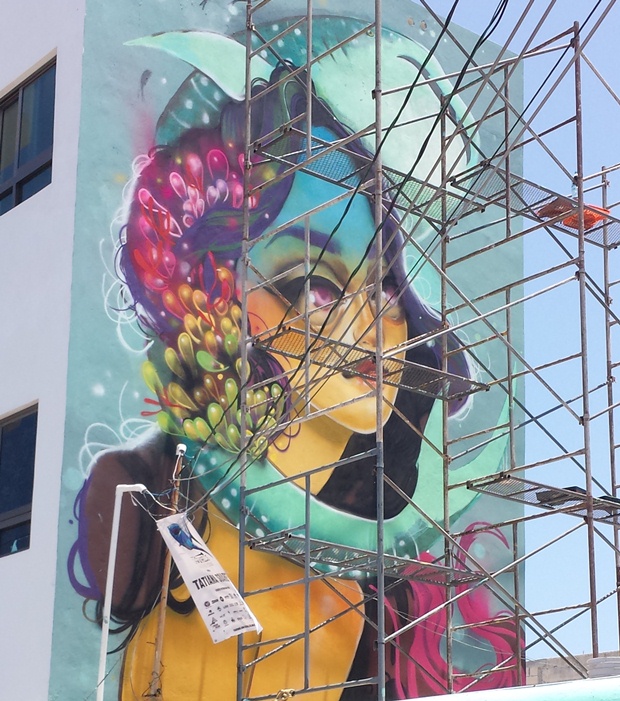 A mural of a whale shark wrapping his body around the head of an enchanting young woman with oval-shapped colors of green and red throughout her hair