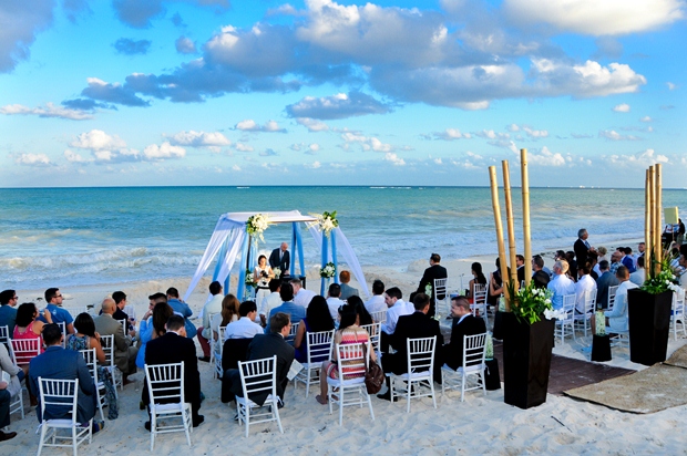 A bride and groom saying their vows at the beach in Cancun before a group of friends and family