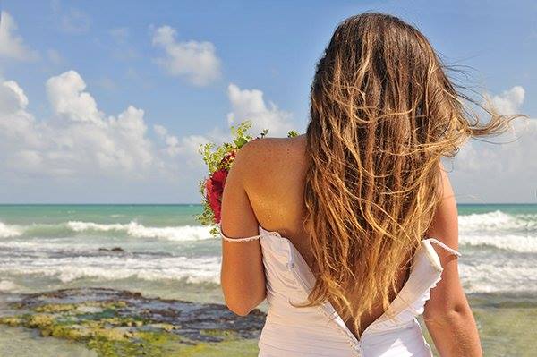 A bride holding a flower arrangement as she looks out to the Caribbean Sea in Mexico's Riviera Maya