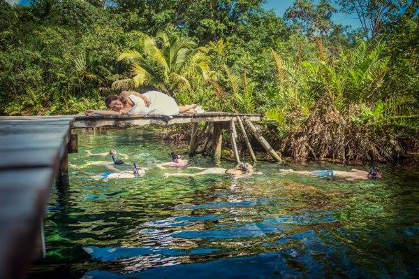 A bride rests upon a pier of a cenote as snorkelers swim by in the Riviera Maya, Mexico