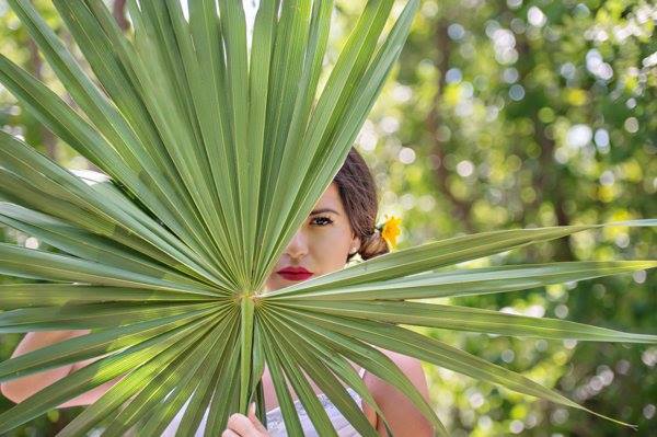 A model peaking out from behind a palm tree branch in the Riviera Maya, Mexico