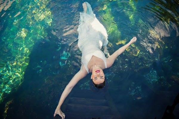 A bridal model holds on to a ladder as she looks up into the camera at a cenote in Mexico's Riviera Maya