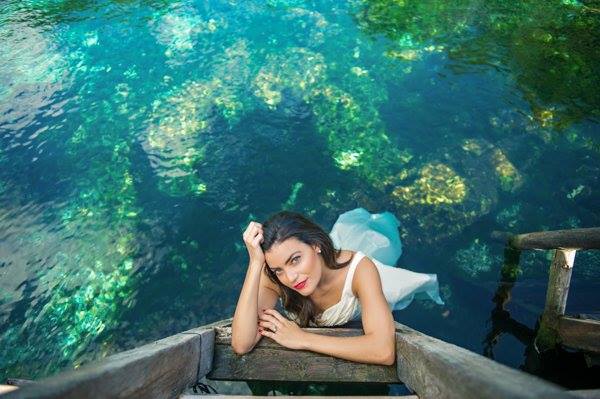 A newlywed bride looking up at the camera from within the cool waters of a Maya cenote in the Mexican Caribbean