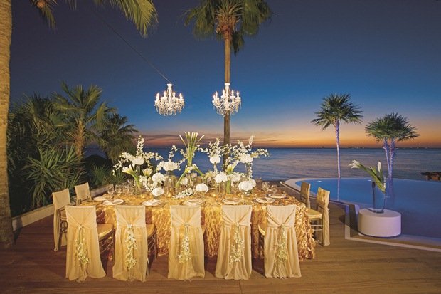 The sun sets over a gold-decorated wedding dinner table at the edge of the beach in the Riviera Maya, Mexico