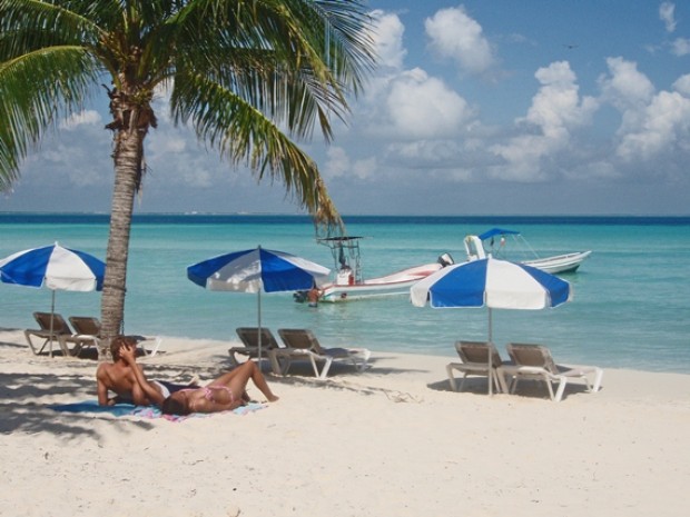 Tourists relax under a palm tree on Isla Mujeres island as part of the numerous Cancun family activities available at this international tourist hub