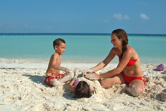 A family playing in the sand on the beach in Cancun during their Mexico Family Vacations