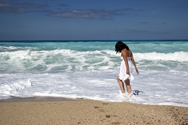 A young woman in a white dress walks barefoot through the Caribbean Sea at Bayahibe beach in La Romana, Dominican Republic