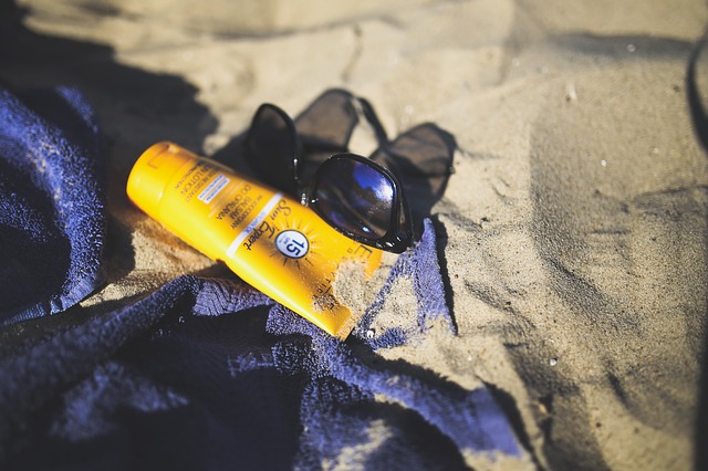 A bottle of sunscreen, sunglasses and a towel lying on a beach