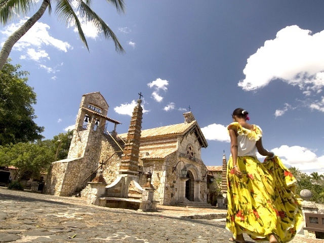 A woman in traditional dress stands before a colonial-style church on the Amstar dmc Santo Domingo City Tour