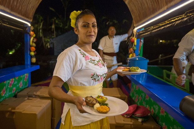 A waitress at Xoximilco serving food aboard a trajinera