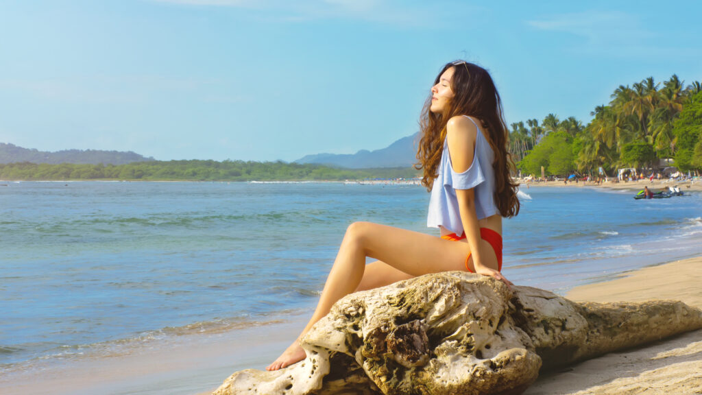 Beautiful Teenage Girl Sitting on Driftwood at a beach in Costa Rica
