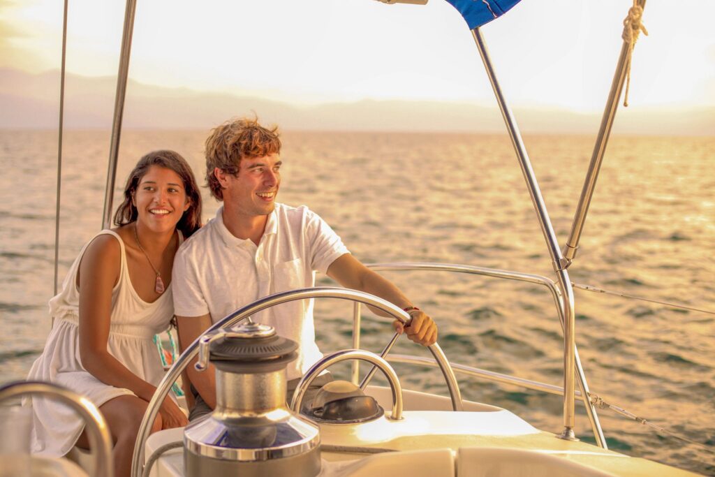 A young couple sails a sailboat at sunset on the calm waters of Los Cabos, Mexico.